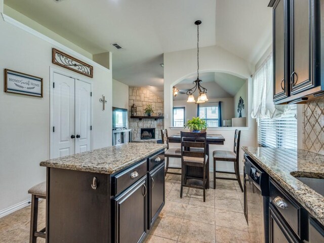 kitchen featuring visible vents, an inviting chandelier, lofted ceiling, a stone fireplace, and black dishwasher