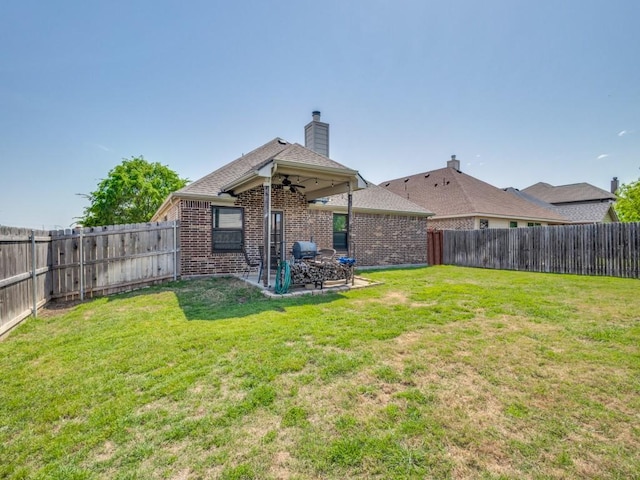 rear view of house featuring a fenced backyard, a ceiling fan, a lawn, and brick siding