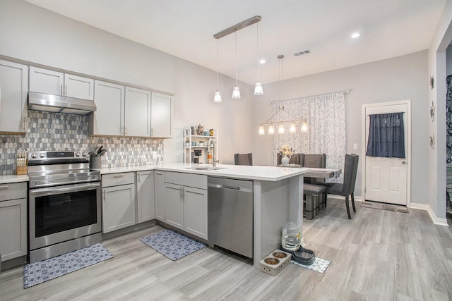 kitchen with stainless steel appliances, under cabinet range hood, a sink, gray cabinetry, and light wood-style floors