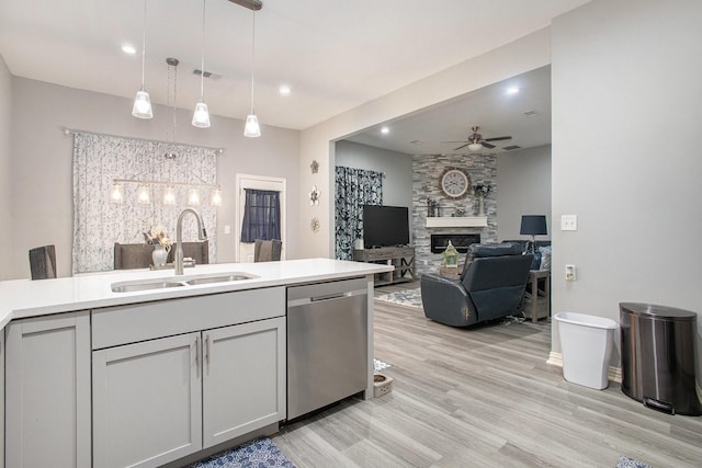 kitchen with stainless steel dishwasher, a sink, a ceiling fan, a large fireplace, and light wood-style flooring