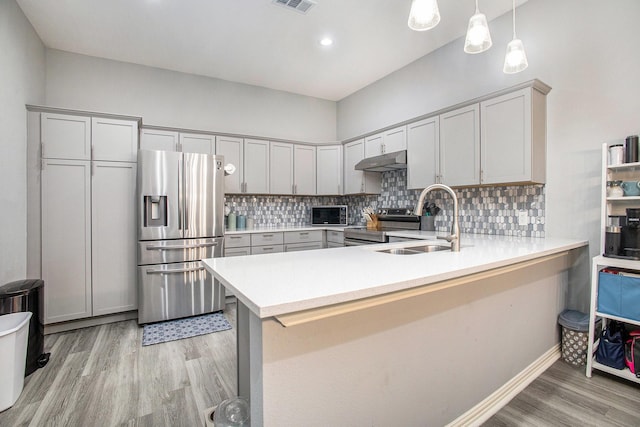 kitchen featuring appliances with stainless steel finishes, under cabinet range hood, a sink, light wood-style flooring, and a peninsula
