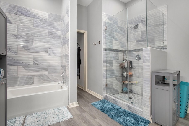 full bathroom featuring a stall shower, wood finished floors, a tub, and baseboards