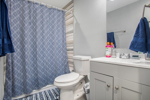 bathroom featuring toilet, vanity, a textured wall, and a shower with curtain