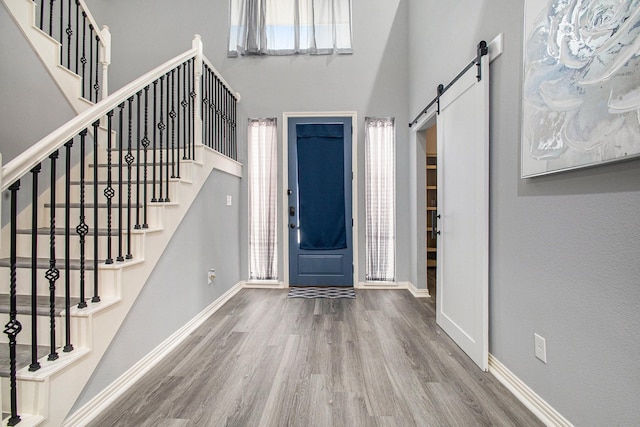 entrance foyer with a barn door, wood finished floors, baseboards, stairs, and a towering ceiling
