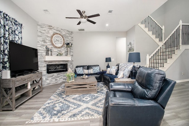 living area with wood finished floors, a ceiling fan, stairway, a stone fireplace, and recessed lighting