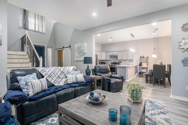 living area featuring light wood-style flooring, stairs, a barn door, recessed lighting, and baseboards