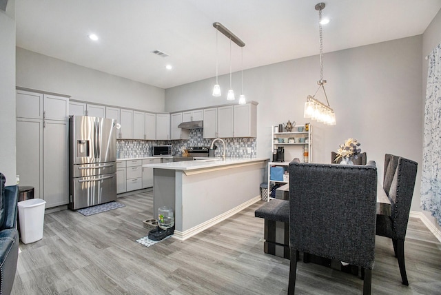 kitchen with stainless steel appliances, a peninsula, light wood-style floors, and decorative backsplash