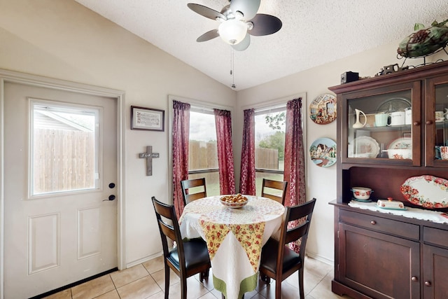 dining area with ceiling fan, a textured ceiling, baseboards, light tile patterned floors, and vaulted ceiling