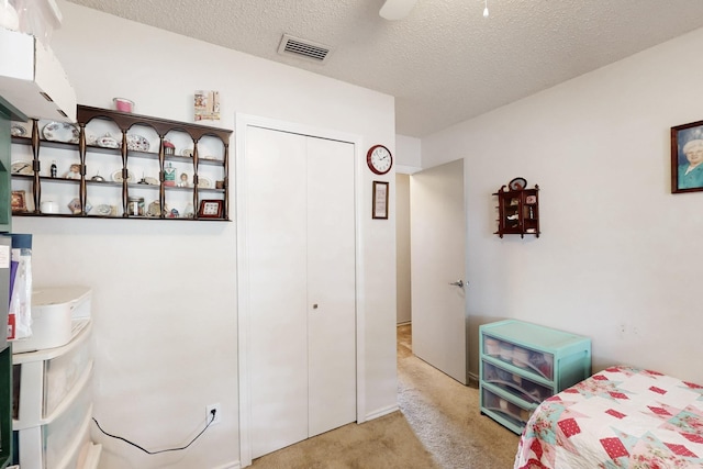 carpeted bedroom featuring ceiling fan, a closet, a textured ceiling, and visible vents
