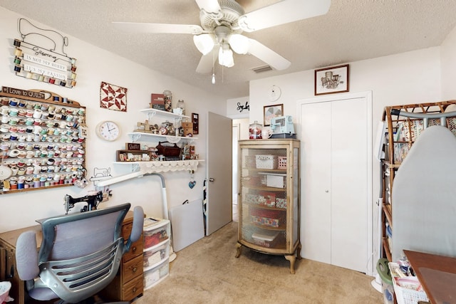 home office with visible vents, a textured ceiling, ceiling fan, and light carpet