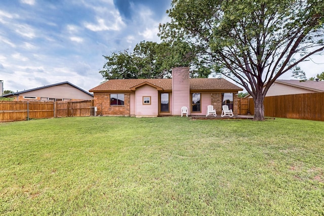rear view of property featuring a fenced backyard, a yard, and a chimney