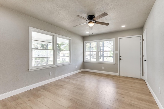 empty room with ceiling fan, light wood finished floors, and a textured ceiling