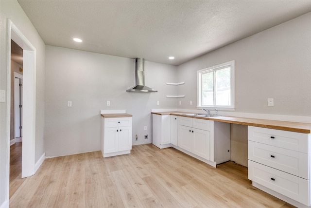 kitchen featuring wall chimney range hood, white cabinets, a sink, light wood-style floors, and recessed lighting