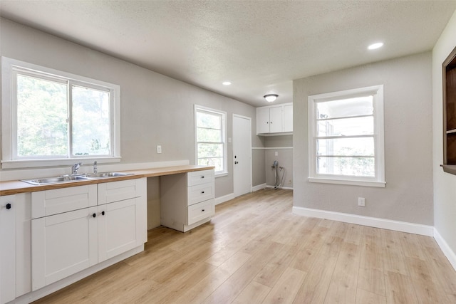 kitchen featuring a textured ceiling, a sink, baseboards, light wood finished floors, and white cabinetry
