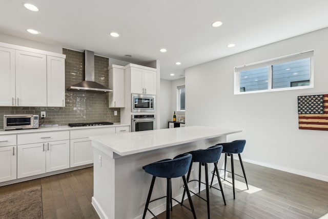 5424 Anita St, Dallas, TX 75206 - kitchen with appliances with stainless steel finishes, wall chimney exhaust hood, a kitchen bar, wood finished floors, and light countertops