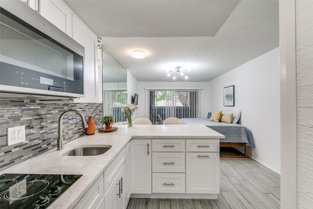 kitchen featuring a peninsula, black electric stovetop, stainless steel microwave, tasteful backsplash, and a sink
