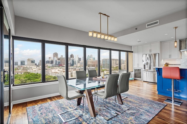 dining area featuring beverage cooler, visible vents, a city view, and light wood finished floors