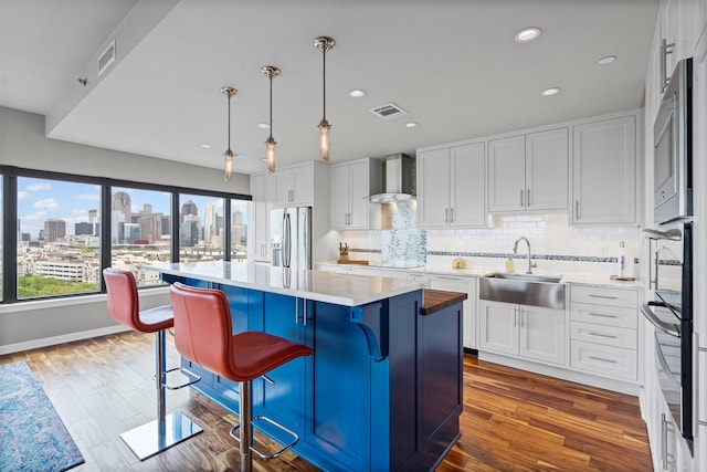 kitchen with wall chimney range hood, a sink, stainless steel fridge with ice dispenser, white cabinetry, and visible vents