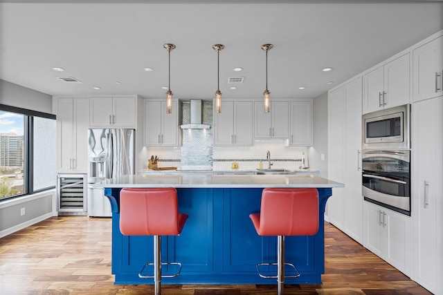kitchen featuring visible vents, wine cooler, wall chimney range hood, a sink, and appliances with stainless steel finishes