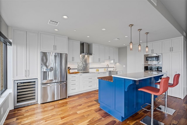 kitchen featuring appliances with stainless steel finishes, a sink, white cabinets, wine cooler, and wall chimney exhaust hood