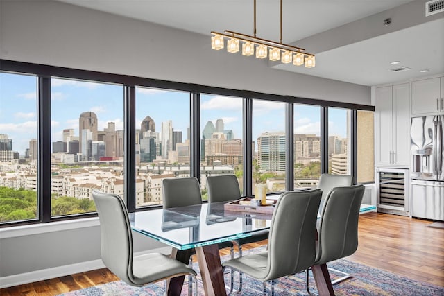 dining space featuring visible vents, a view of city, wine cooler, baseboards, and light wood-type flooring
