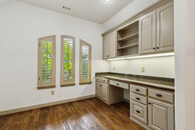unfurnished office featuring baseboards, dark wood finished floors, built in desk, and visible vents