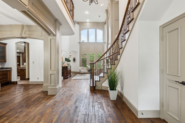 entryway with stairs, a towering ceiling, baseboards, arched walkways, and dark wood finished floors