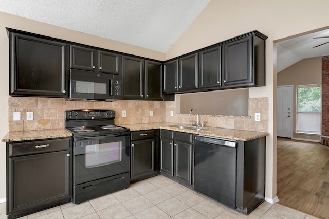 kitchen with vaulted ceiling, light stone counters, black appliances, and a sink