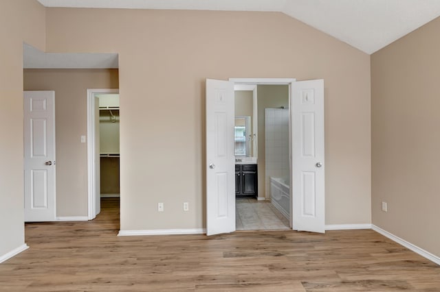 unfurnished bedroom with connected bathroom, a walk in closet, baseboards, lofted ceiling, and light wood-type flooring