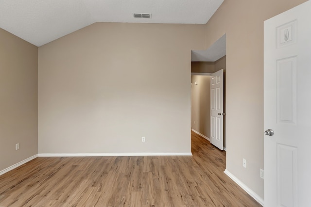 empty room featuring baseboards, visible vents, vaulted ceiling, and light wood-type flooring
