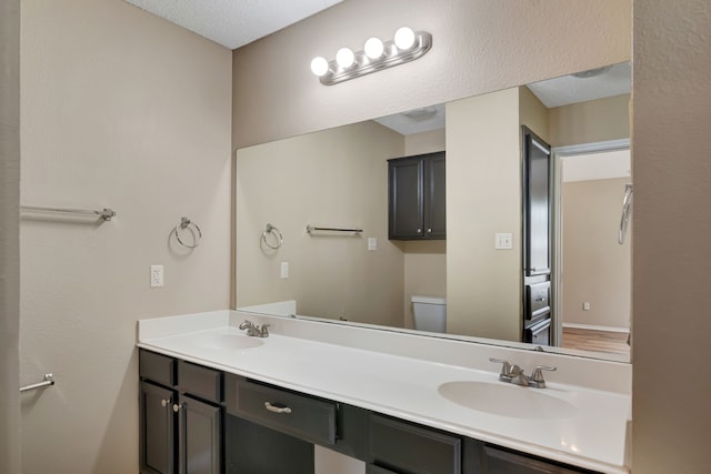bathroom with a sink, a textured ceiling, toilet, and double vanity