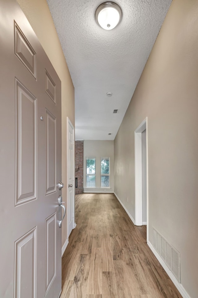 hallway featuring visible vents, baseboards, a textured ceiling, and wood finished floors