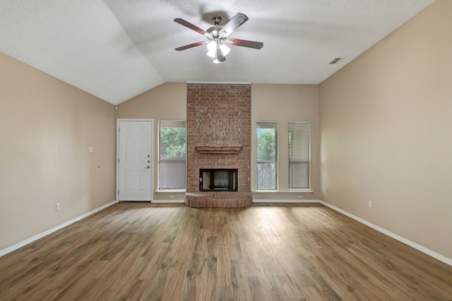 unfurnished living room with a ceiling fan, visible vents, a brick fireplace, wood finished floors, and baseboards