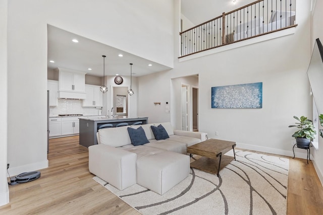 living area with light wood-style floors, recessed lighting, baseboards, and a towering ceiling