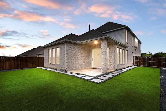 back of house at dusk with a lawn, brick siding, a patio, and a fenced backyard