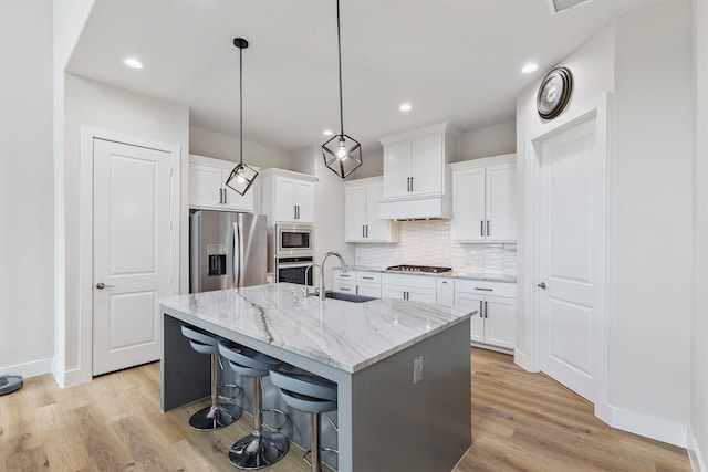 kitchen with decorative backsplash, an island with sink, a sink, light wood finished floors, and stainless steel appliances