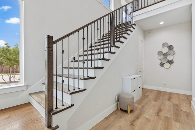 stairs with baseboards, plenty of natural light, wood finished floors, and a towering ceiling