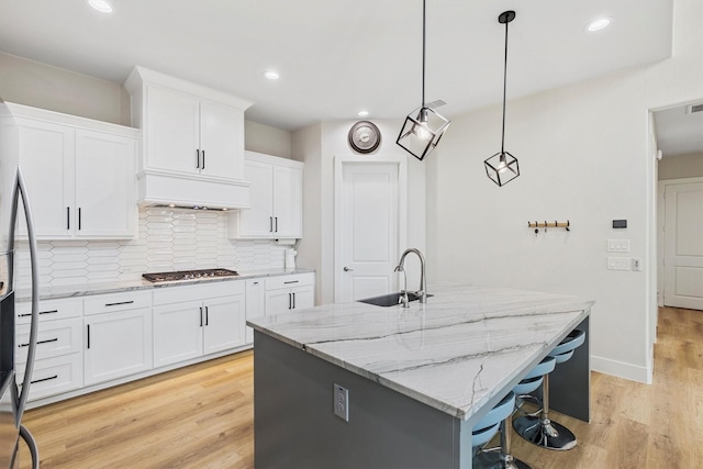 kitchen featuring white cabinets, a sink, light wood finished floors, tasteful backsplash, and custom exhaust hood