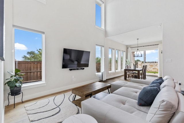 living area with baseboards, a high ceiling, a notable chandelier, and wood finished floors
