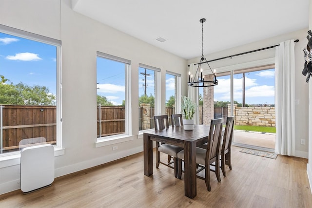 dining space featuring light wood-style floors, baseboards, a healthy amount of sunlight, and a notable chandelier