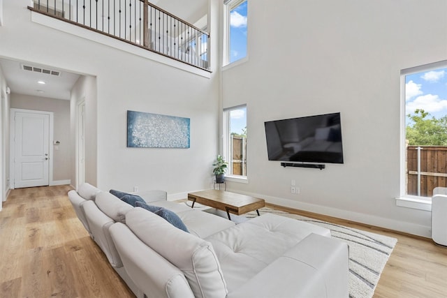 living area featuring visible vents, a high ceiling, baseboards, and wood finished floors