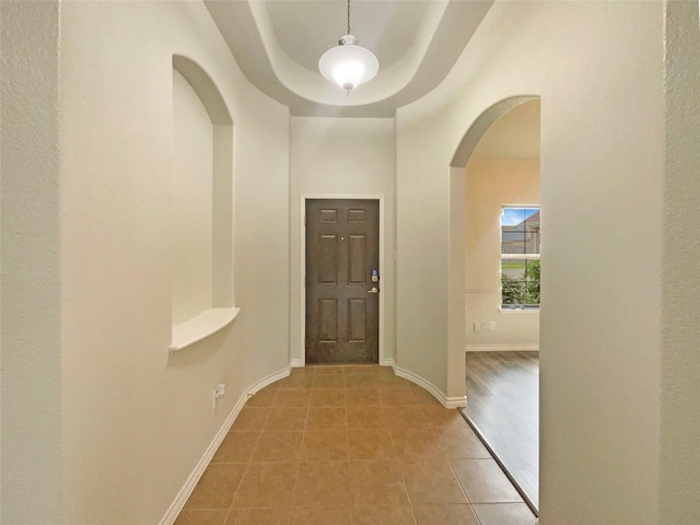 entrance foyer featuring light tile patterned floors, arched walkways, and baseboards