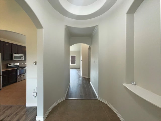 hall featuring arched walkways, baseboards, and tile patterned flooring