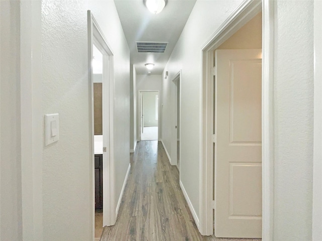 hallway with baseboards, a textured wall, wood finished floors, and visible vents