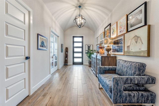 foyer entrance with baseboards, vaulted ceiling, light wood-style flooring, and a notable chandelier