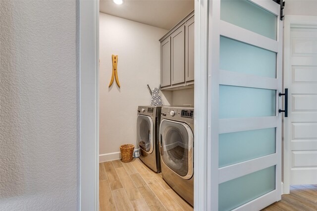 laundry area with cabinet space, light wood-type flooring, a barn door, and washer and dryer