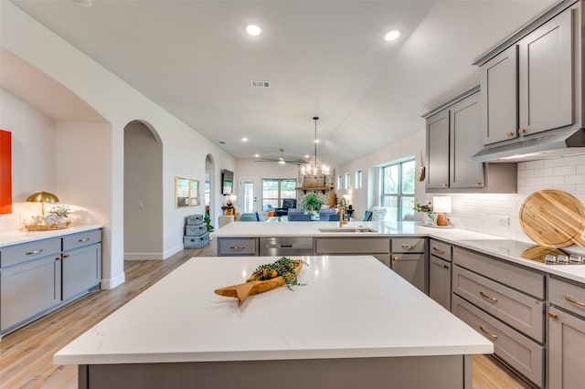 kitchen featuring arched walkways, gray cabinetry, a sink, black electric stovetop, and open floor plan