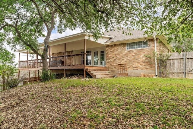 rear view of property featuring fence, brick siding, a wooden deck, french doors, and a lawn