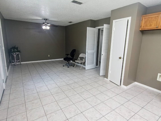 empty room with a ceiling fan, a textured ceiling, visible vents, and light tile patterned floors