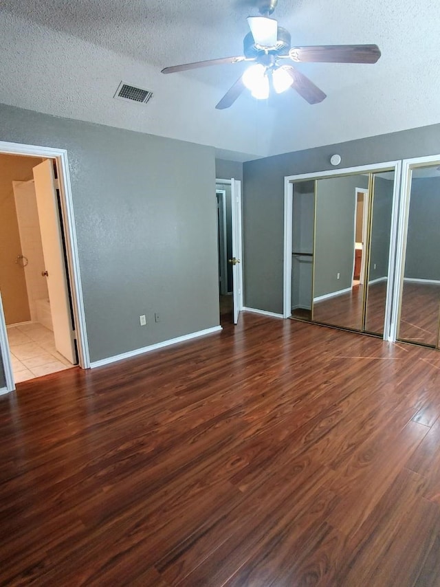 unfurnished bedroom with a textured ceiling, two closets, baseboards, wood finished floors, and visible vents